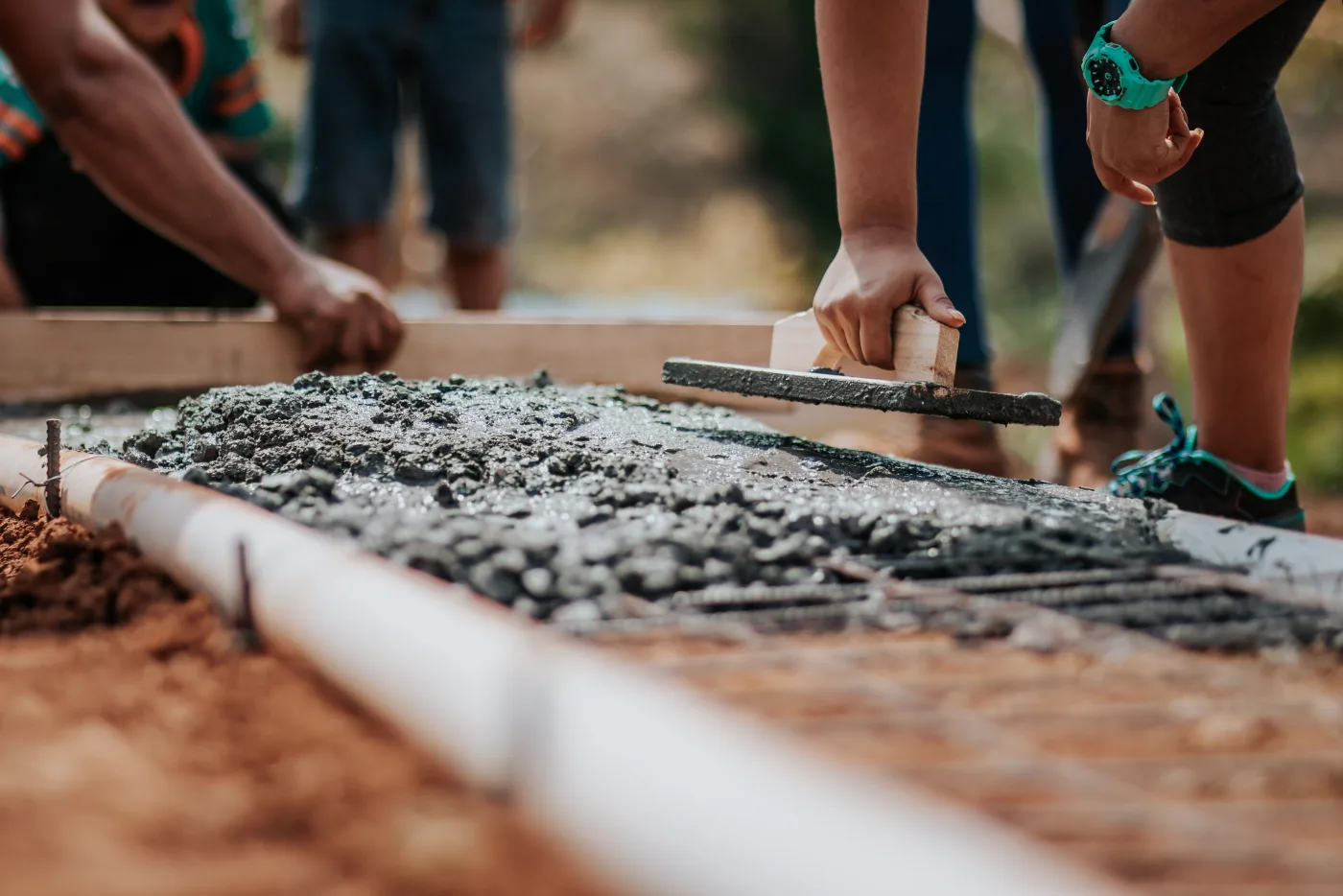 Close view of a hand float drawn across fresh concrete inside wood forms, a rebar mat visible just below the surface