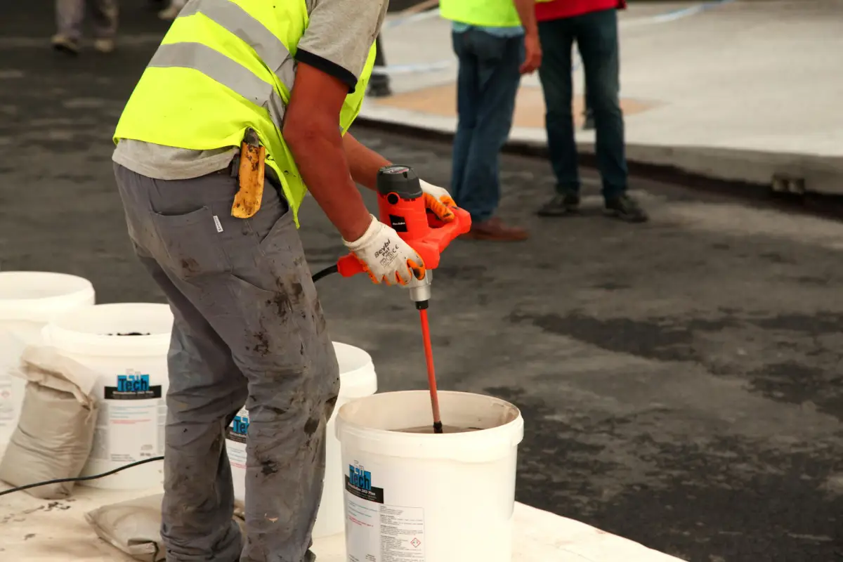 Worker in a high-visibility vest mixing repair mortar in a bucket