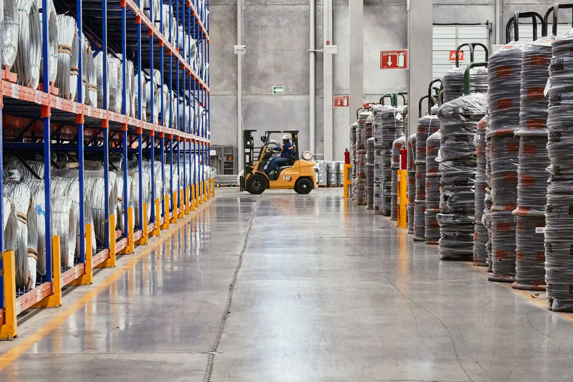 Warehouse racking loaded with product standing on a concrete floor, a forklift working the aisle