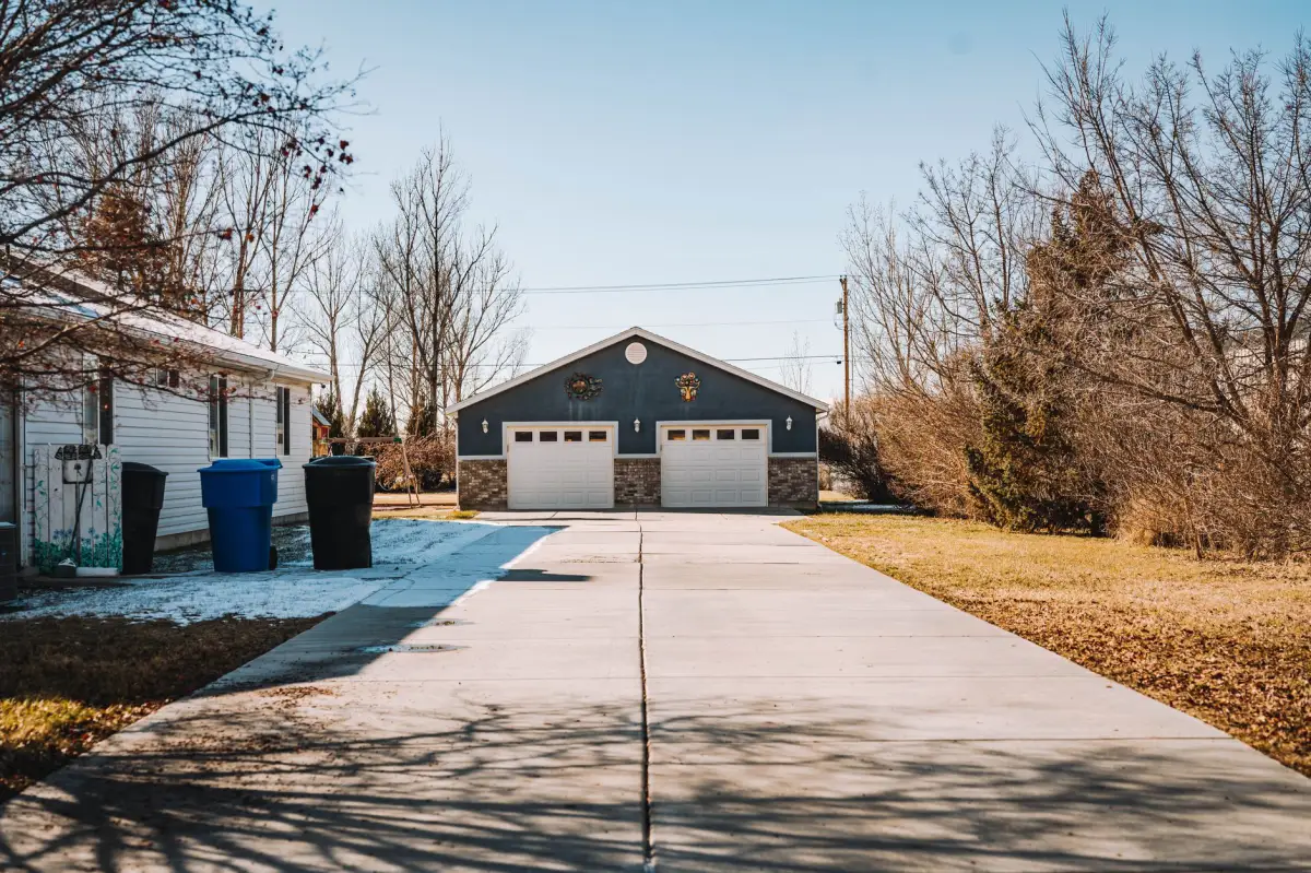 Long concrete driveway leading back to a detached garage, bare trees along the lot line