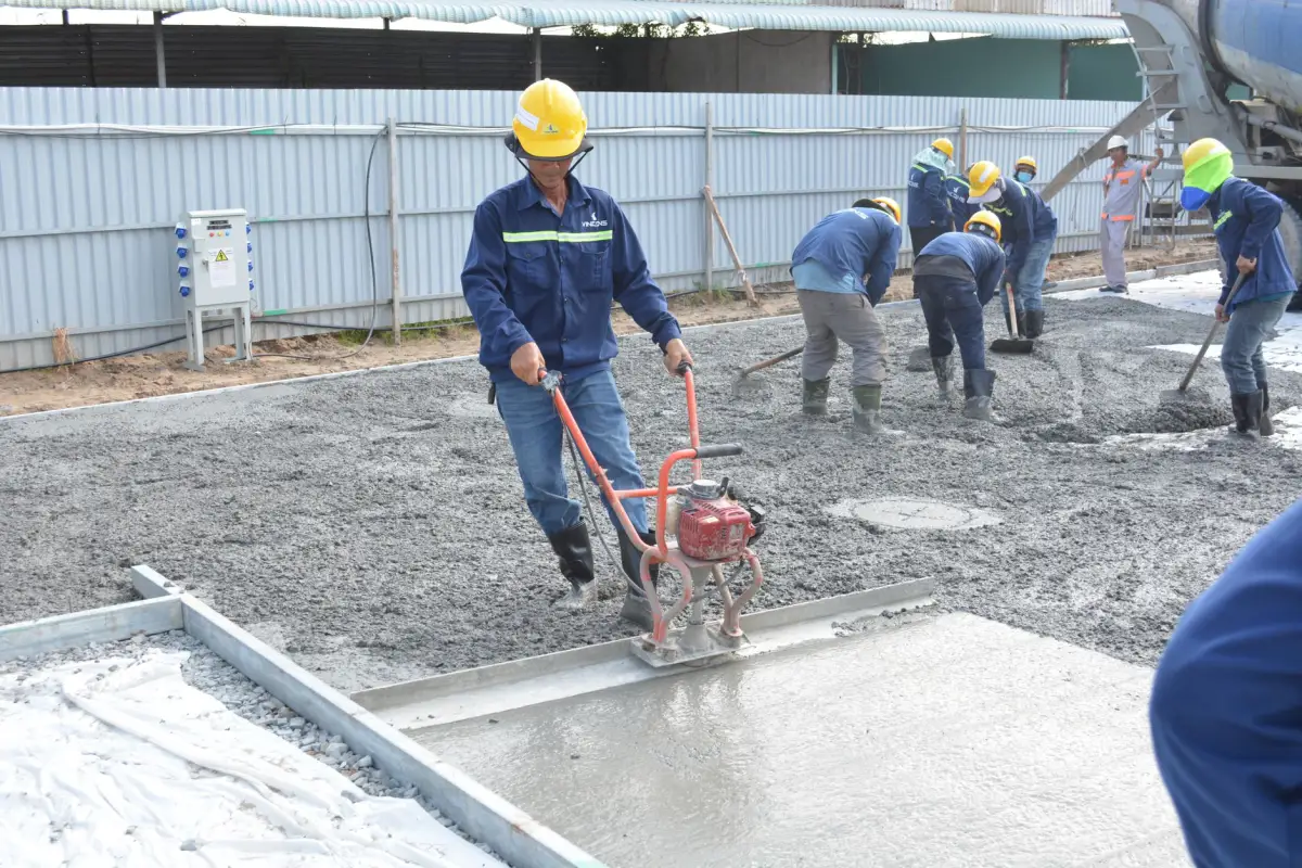 Worker in a hard hat running a power screed along a freshly placed concrete strip