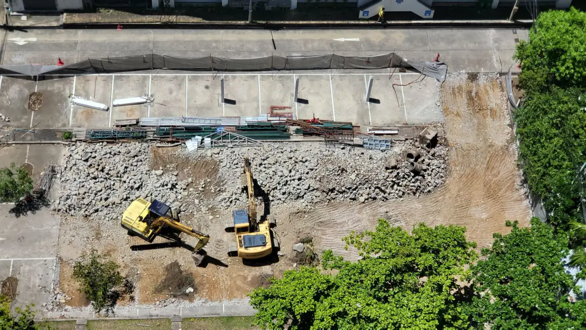 Excavator working a strip of ground beside a concrete wall during removal