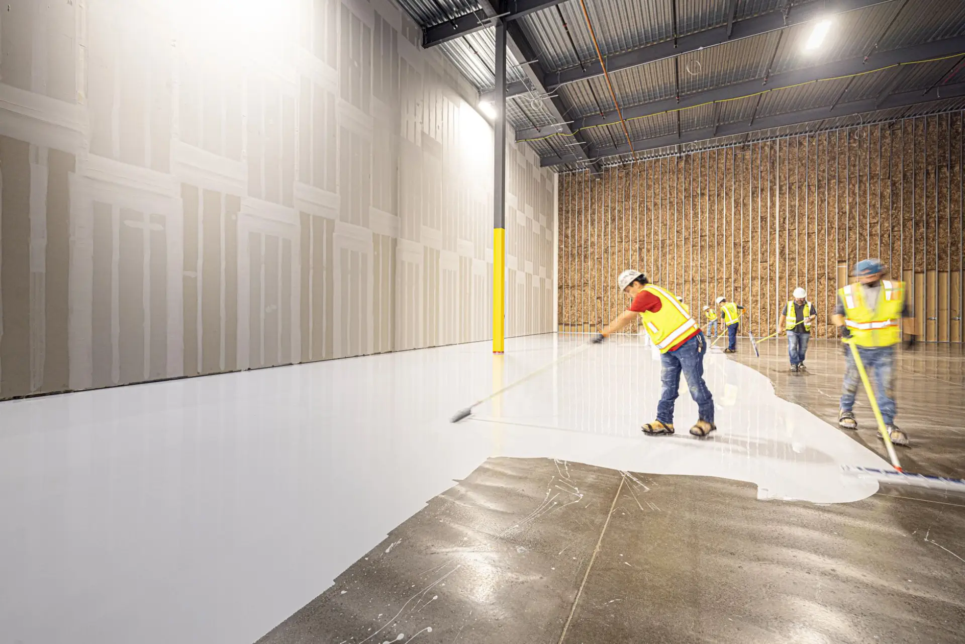 Crew in high-visibility vests spreading an overlay coating across a new warehouse floor