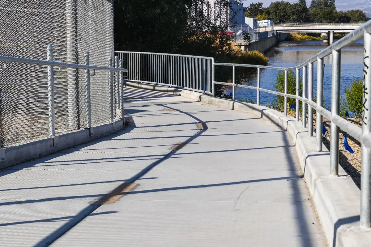 Concrete walkway with a metal railing curving alongside water