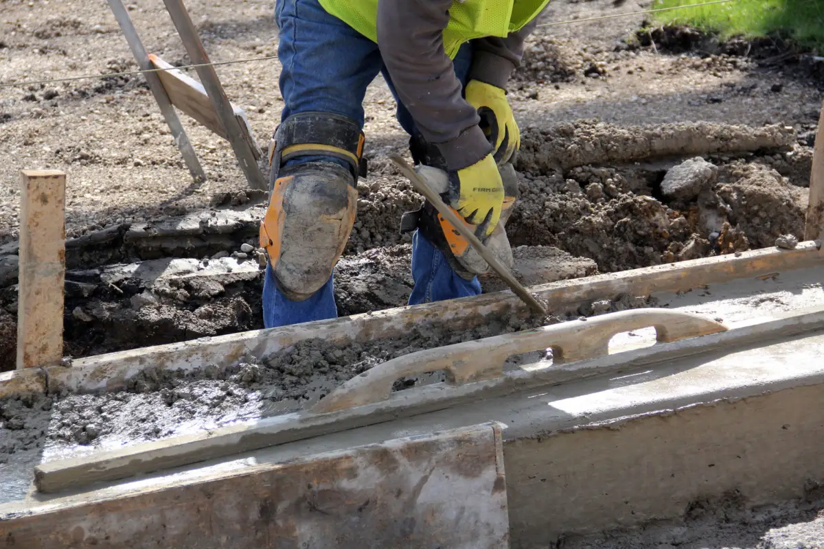 Gloved hands tooling the edge of freshly placed concrete along a formed curb