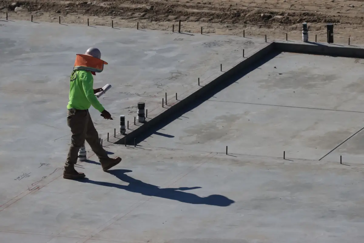 Worker walking a large fresh concrete slab beside the formed edge