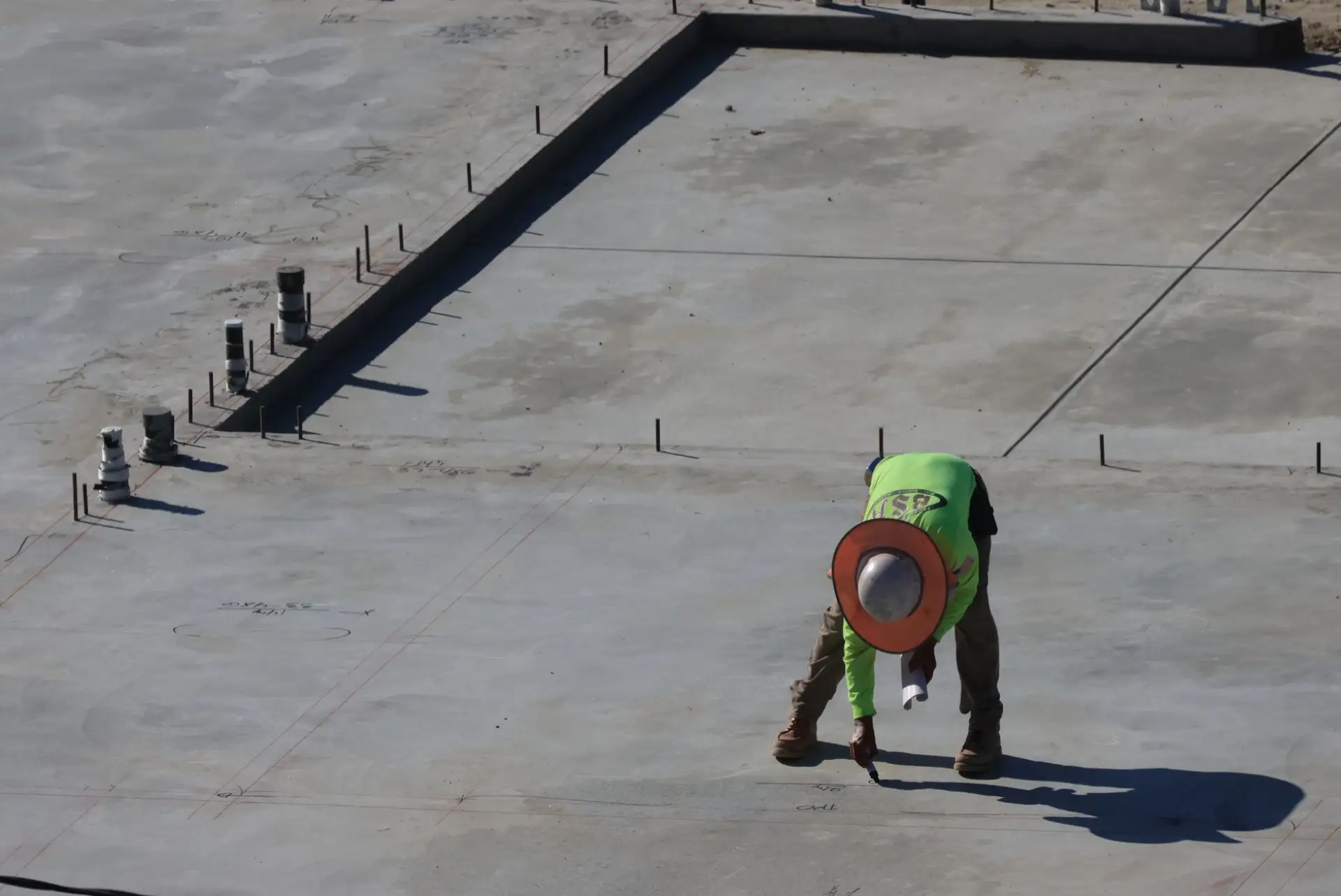 Worker in high-visibility clothing standing on a large freshly placed concrete slab inside its edge forms